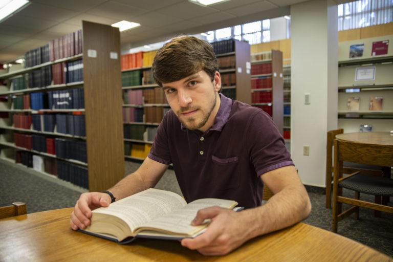 Nick Vaporciyan sits at a wooden table and looks up from a book.