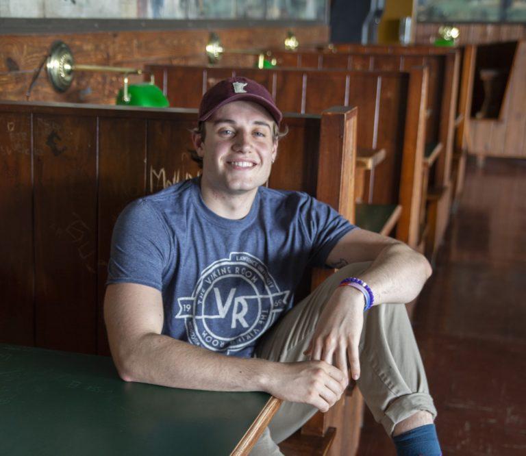 Liam Wulfman, wearing a VR T-shirt, sits in a wooden booth.