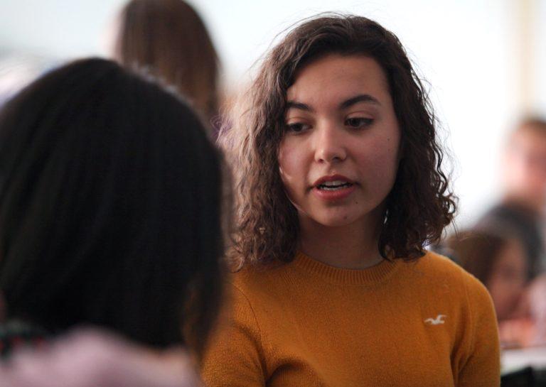 Sophie Dion-Kirschner, wearing a yellow sweater, speaks to a dark-haired girl.