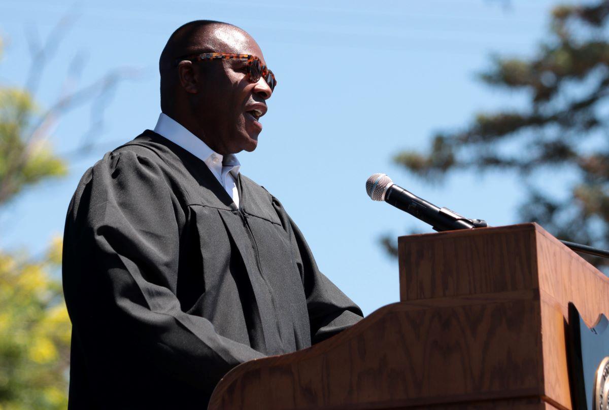 Nettles behind a podium, wearing academic regalia and sunglasses