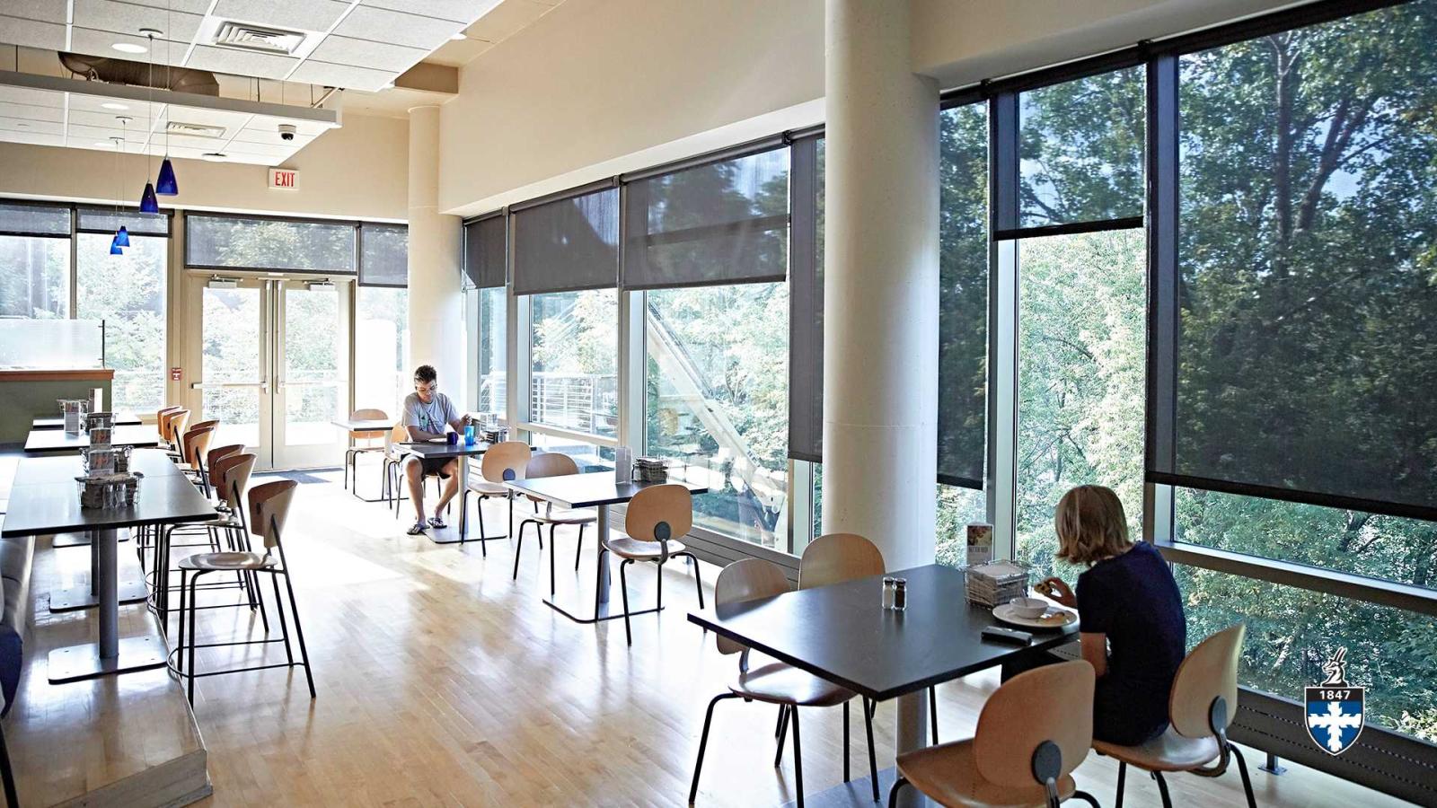 Students sitting near window in cafeteria eating.