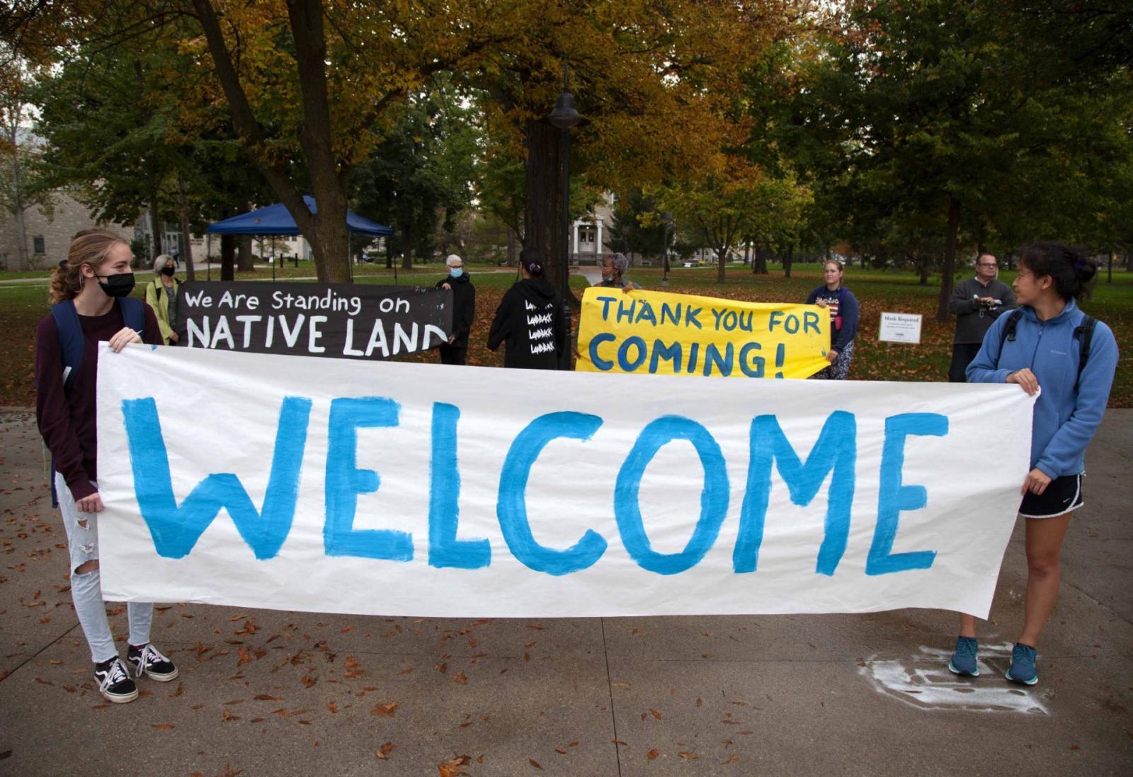 Students hold signs that say "welcome", "Thank you for coming!" and "we are standing on native land" during the university's 6th Annual Indigenous Peoples' Day Celebration.