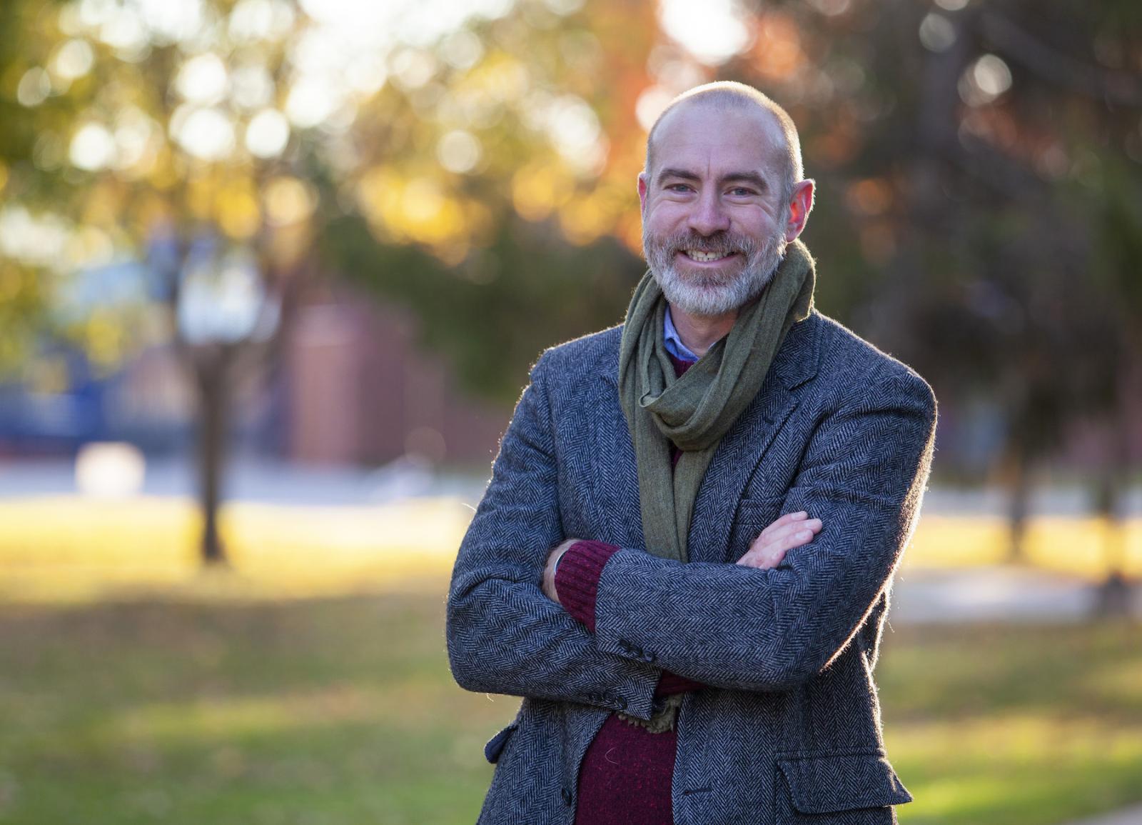 Jason Brozek, wearing a grey tweed blazer, stands on Main Hall Green. 