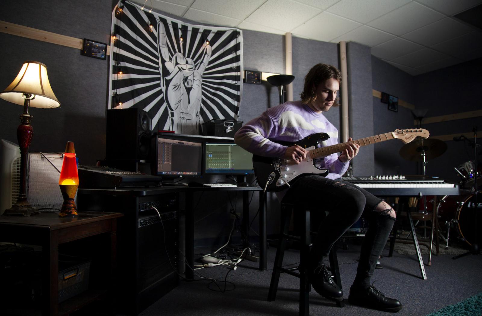 Michael Murphy, surrounded by instruments and recording equipment, plays the electric guitar.