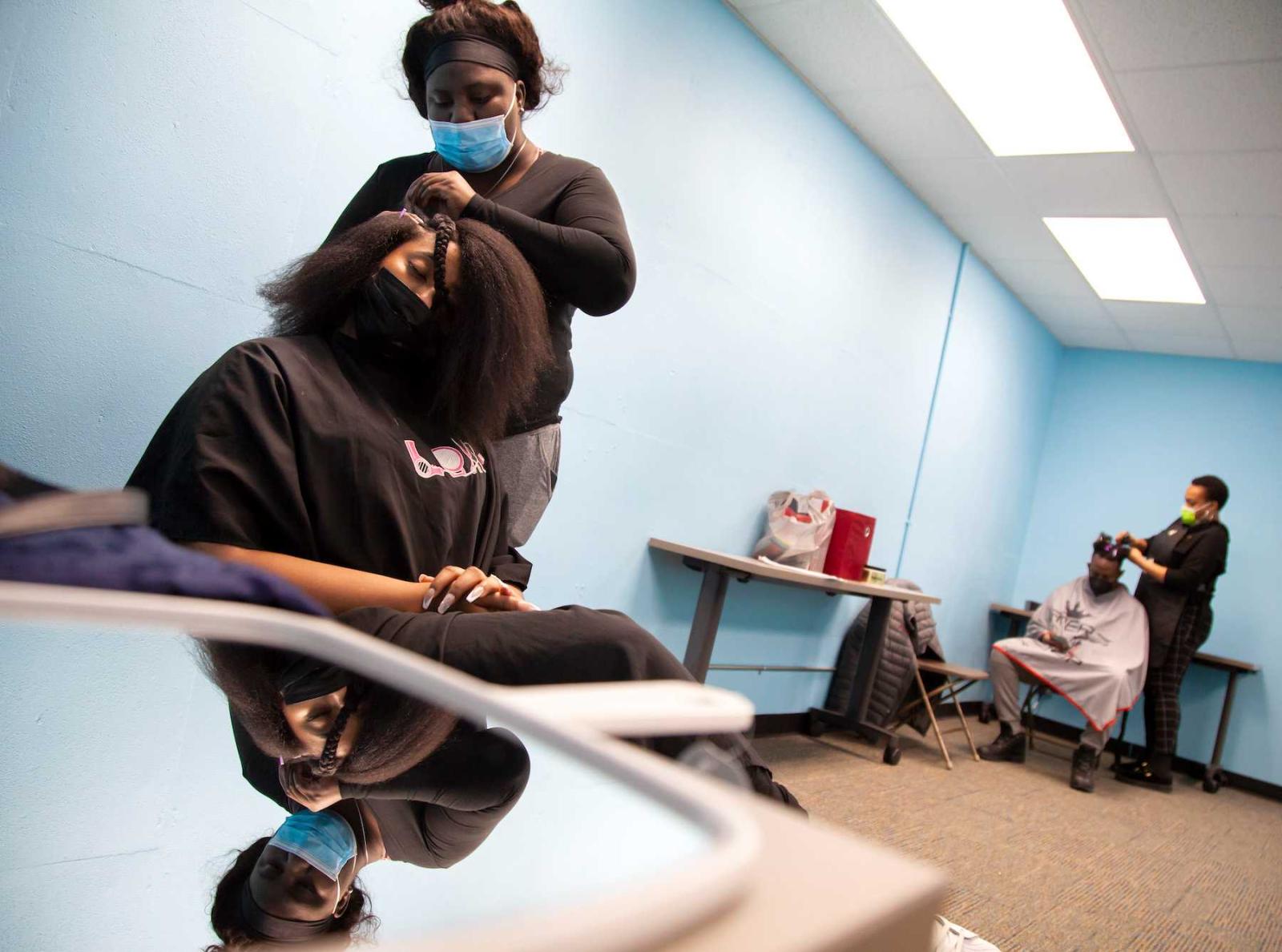 Kieta Pritchard, with City’s Best Braids, braids the hair of Kelsi Bryant as another stylist works on the hair of another student in the background. 