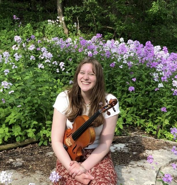 Mallory Welsch holds a viola in front of flowers.