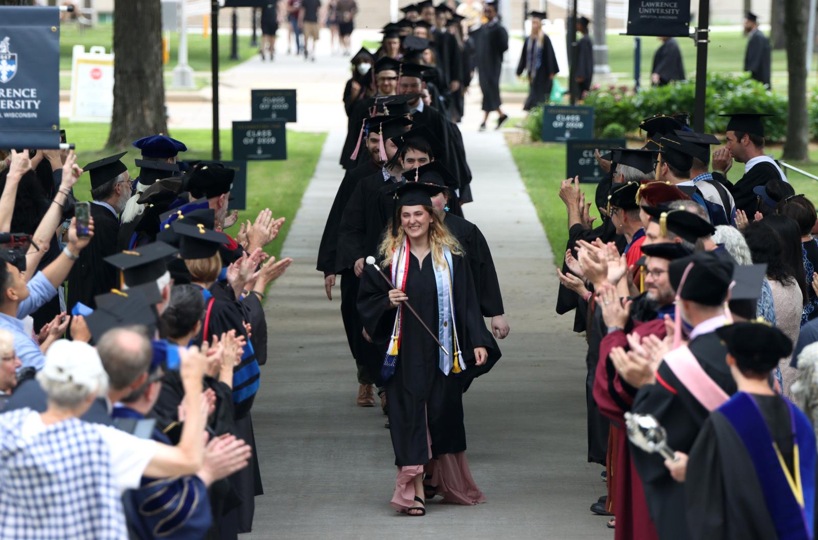 Graduates dressed in cap and gown process between rows of faculty dressed in regalia.