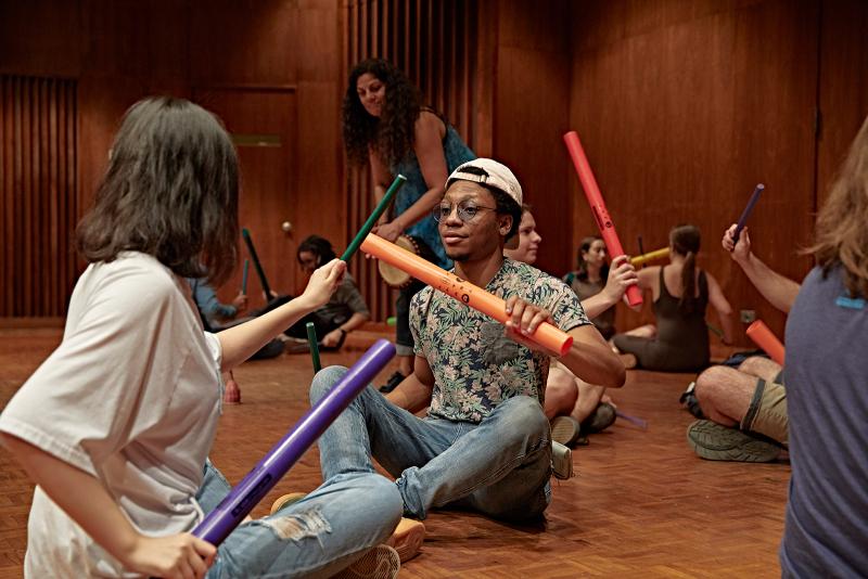 A large group of students playing with boomwhackers while seated on the floor.