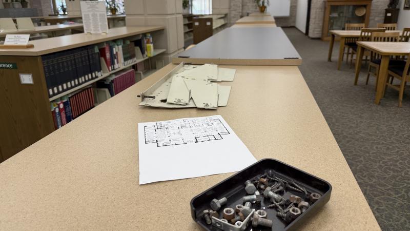 Top of a shelf on the first floor of the library with nuts and bolts in a tray, a printed floorplan, and small metal shelf parts.