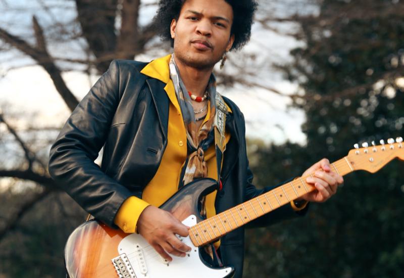 Buddy Red looks at the camera holding an electric guitar.