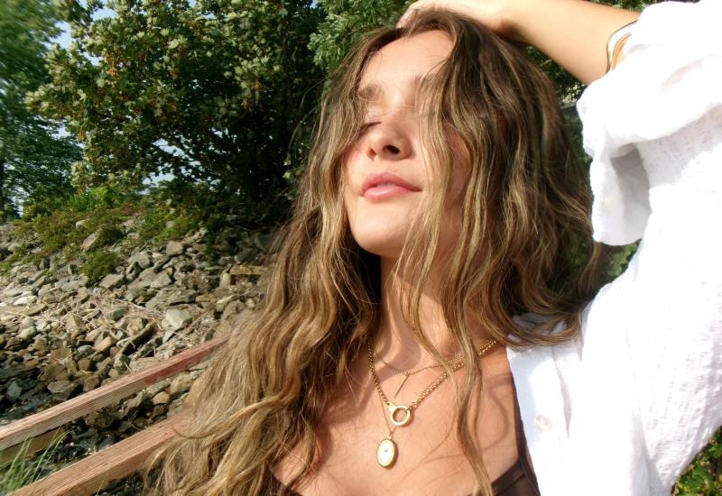 Ruby Mac poses on a bridge looking up towards the sky with her eyes closed.