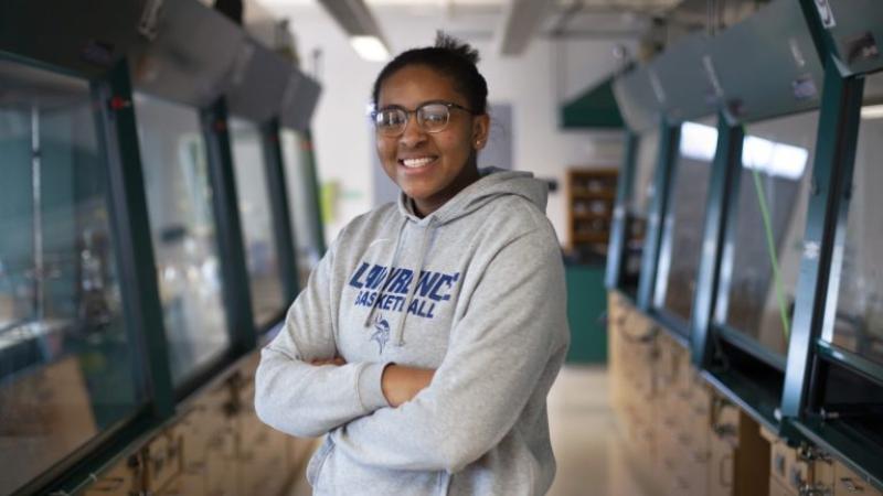 Kenya Earl, wearing a grey Lawrence basketball sweatshirt, stands with her arms crossed and smiles at the camera.