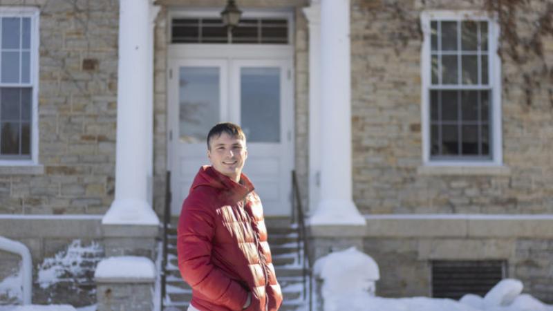 Andrew Sage, wearing in a red winter coat, stands in front of Main Hall.