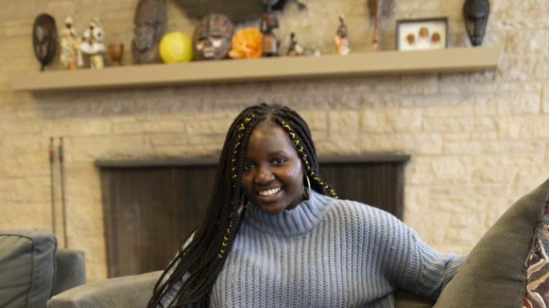 Awa Badiane, wearing a grey sweater and blue jeans, sits on a circular lounge chair and smiles at the camera.