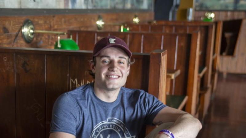 Liam Wulfman, wearing a VR T-shirt, sits in a wooden booth.