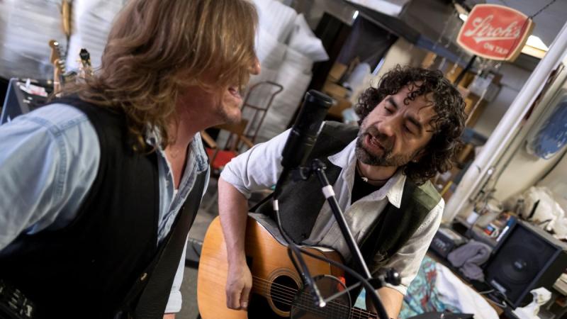 Rob Neilson and Jake Frederick playing the guitar and singing into a mic 
