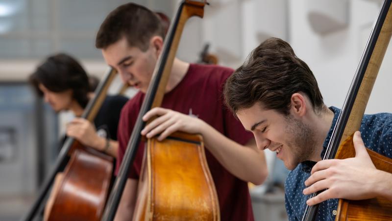 A small group of students playing upright basses in class.