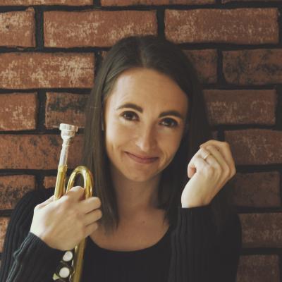 Jessica Jensen holding a trumpet in front of a brick wall