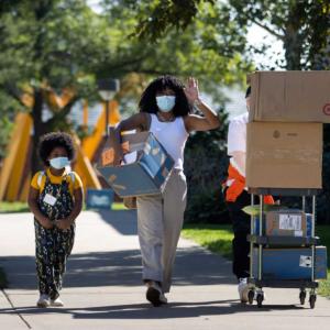 Student walk down sidewalk with luggage and family.