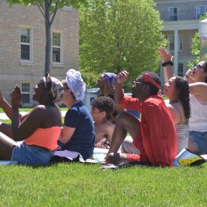 Group of students sitting on lawn of the Quad, clapping.