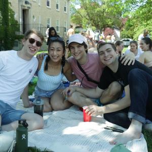 Four students sitting on a blanket on the grass outside the Quad.