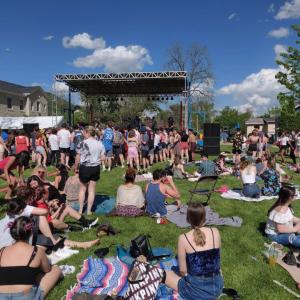 Students sitting in pods across the lawn in front of a stage on a bright sunny day. 