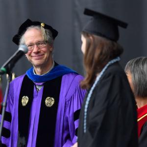 Faculty smiles at student stands on stage.