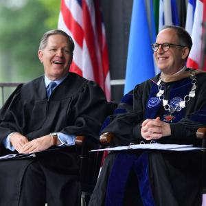 Former President Mark Burstein sits on stage with colleague as they chat and laugh.