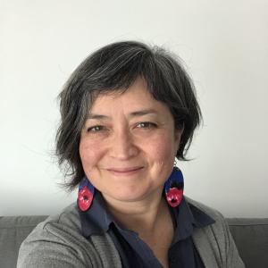 head shot of smiling, mixed race Asian woman in blue shirt collar with grey sweater and red flower earrings